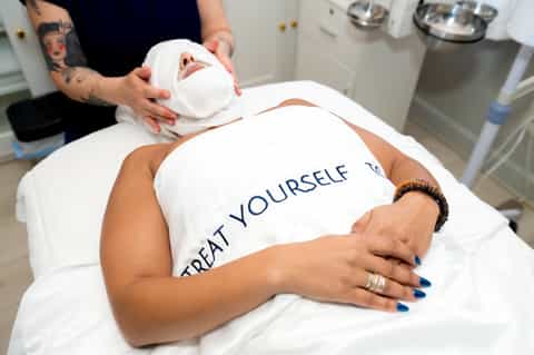 Spa treatment room with therapist applying facial mask to client wearing white towel
