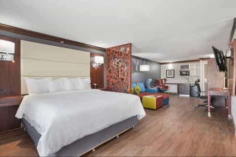 Modern hotel suite with king bed, decorative wooden screen, seating area, and work desk