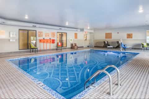 Bright indoor swimming pool with lane markings, deck seating, and glass-walled observation areas
