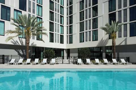 Resort pool with turquoise water, palm trees, white lounge chairs, and modern white building