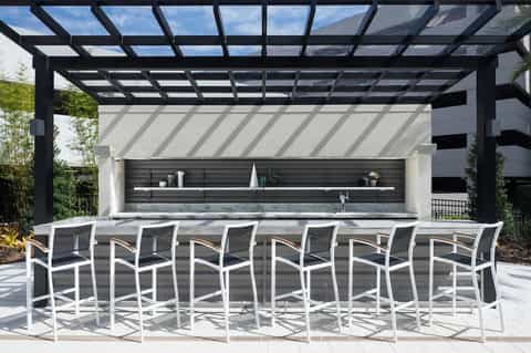 Outdoor bar with pergola, dark frame, white bar stools, and stainless steel countertop