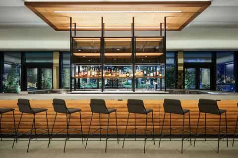 Modern hotel bar with wooden counter seating, illuminated liquor shelves, and contemporary design elements