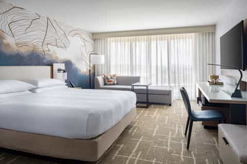 Luxury hotel room with king bed, modern artwork, seating area, and ocean-view balcony