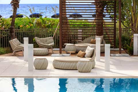 Luxury beachfront lounging area with woven seating pods, ocean view, and tropical landscaping