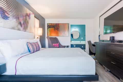 Modern hotel bedroom with queen bed, colorful accents, and teal bathroom entrance
