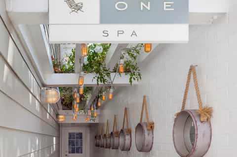 Modern spa entrance with white walls, hanging rope mirrors, greenery, and warm ambient lighting