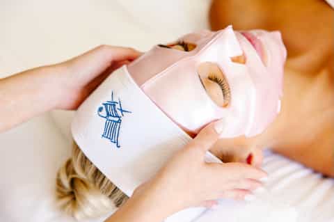 Spa treatment close-up showing facial mask application with brand emblem on wrapped towel