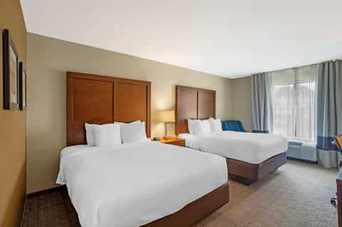 Double queen hotel room with wood headboards, warm lighting, and contemporary furnishings