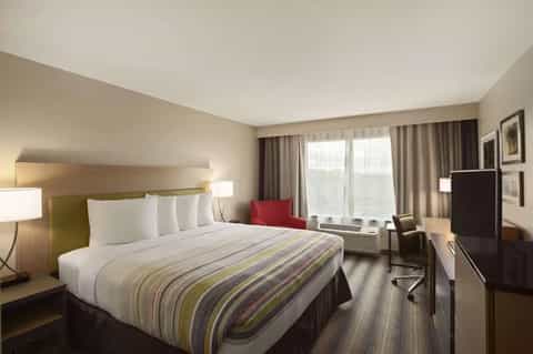 Hotel guest room with queen bed, striped bedding, desk, and large window with city view