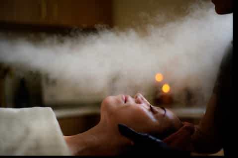 Person receiving spa treatment with steam and candlelight in relaxation setting