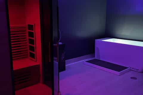 Modern spa treatment room with purple lighting, sauna, and soaking tub