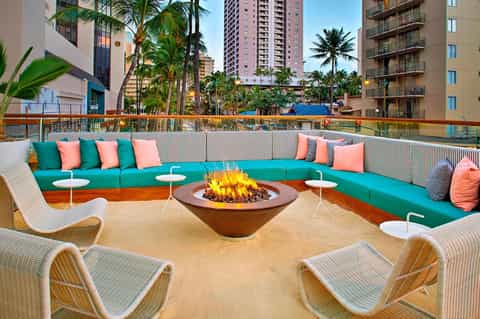 Rooftop lounge with turquoise seating, fire pit, palm trees, and colorful coral accent pillows
