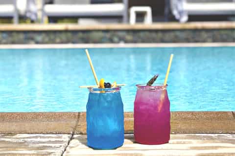 Two colorful cocktails with straws poolside by a resort swimming pool