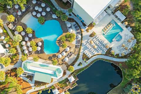 Aerial view of resort with multiple pools, lounge chairs, umbrellas, and surrounding landscaping