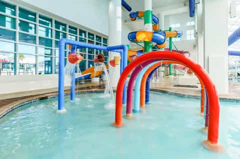 Indoor water park with colorful splash pad structures in bright blue, red, and yellow pipes for children