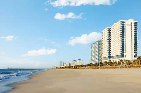 Beachfront resort high-rise building on sandy beach with palm trees and ocean view under clear sky