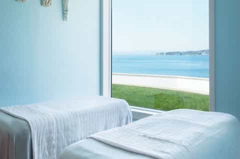 Beachfront hotel bedroom with light blue walls, white bedding, and ocean view from large windows