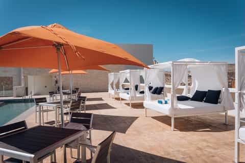 Modern rooftop pool area with large orange umbrella, white cabanas, loungers, and contemporary architecture