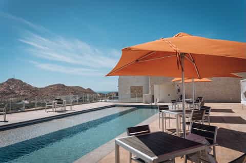 Rooftop pool with orange umbrellas, ocean view, desert mountains, modern architecture, and seating