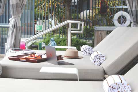 Modern terrace lounge area with white cushioned seating, laptop, food tray, and city views