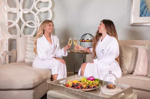 Spa suite with two women in robes enjoying champagne and fruit platter