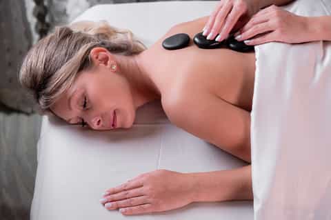 Spa therapist applying heated black stones to client's back during massage treatment