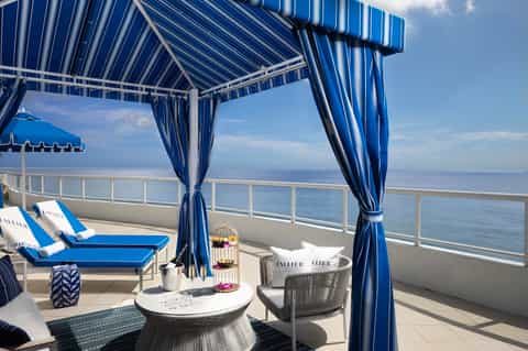 Oceanview balcony cabana with blue striped awning, lounge chairs, and water views