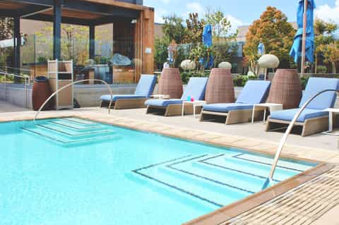 Contemporary pool area with woven loungers, blue cushions, and spa pods overlooking manicured grounds