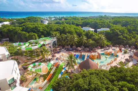 Aerial view of beachside water park with colorful slides, pools, palm trees, and ocean view