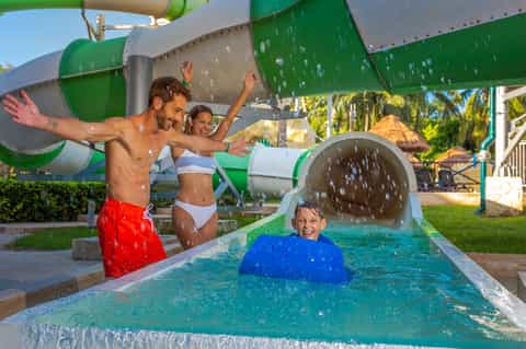 Water park with family on water slide, child in pool with inflatable, tropical backdrop