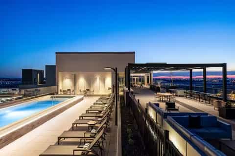 Rooftop pool and lounge at night with city skyline views, modern architecture, and ambient lighting