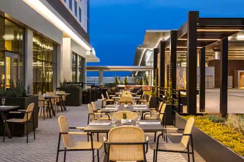 Modern rooftop terrace with dining tables, ocean view at dusk, black pergolas