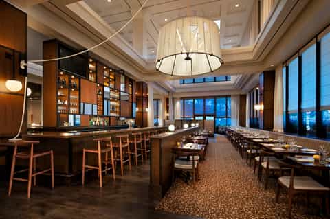 Fine dining restaurant interior with wood bar, elegant lighting, and floor-to-ceiling windows