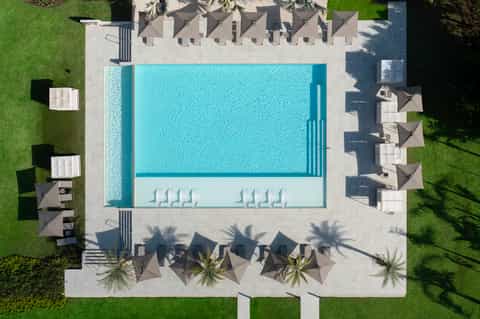 Aerial view of rectangular pool with surrounding lounge chairs and dark umbrellas on concrete patio