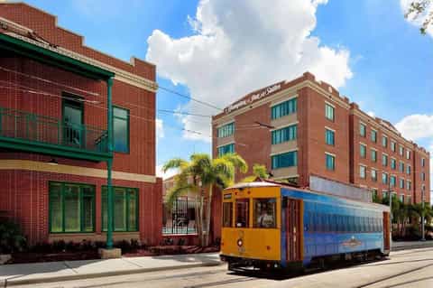 Historic red brick hotel building with colorful street car trolley and palm trees in front