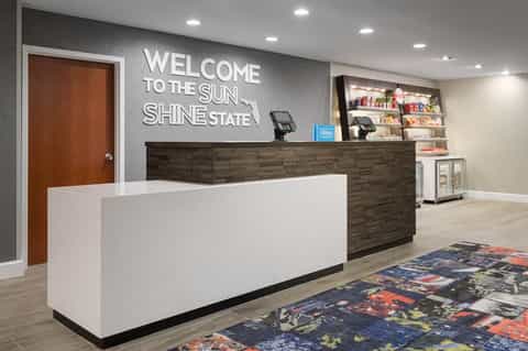 Hotel lobby reception desk with 'Welcome to the Sunshine State' sign and merchandise shelving
