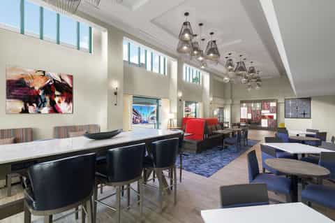 Modern hotel lobby with high ceilings, pendant lights, dining area, and lounge seating