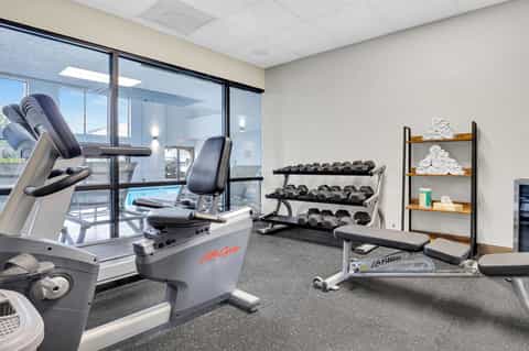 Hotel fitness center with cardio equipment, dumbbells, and window views of pool area