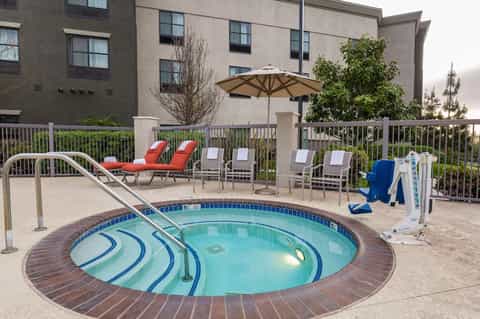 Spa hot tub surrounded by lounge chairs and umbrellas with resort building backdrop
