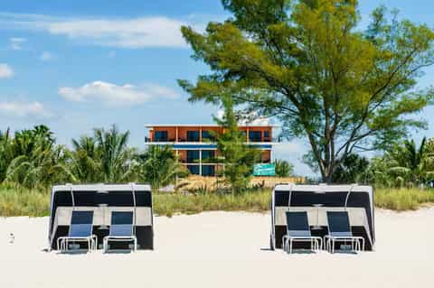 Modern beachfront resort building with orange and blue facade, palm trees, and beach cabanas