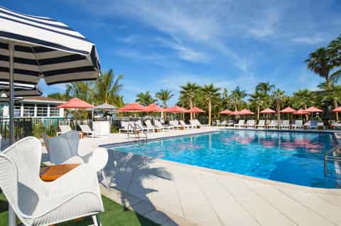 Resort pool with red umbrellas, lounge chairs, and tropical palm trees