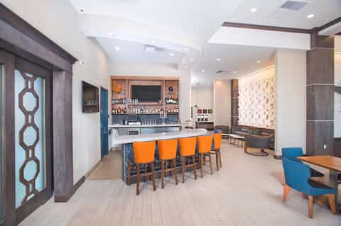 Upscale hotel bar with orange bar stools, modern lighting, wood accents, and sophisticated lounge seating