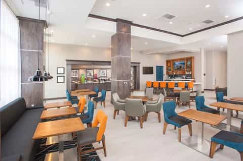 Hotel restaurant and bar with wood tables, blue and orange chairs, service counter, and lounge seating
