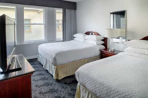 Double queen hotel room with two beds, dark wood furniture, windows, and clean modern decor