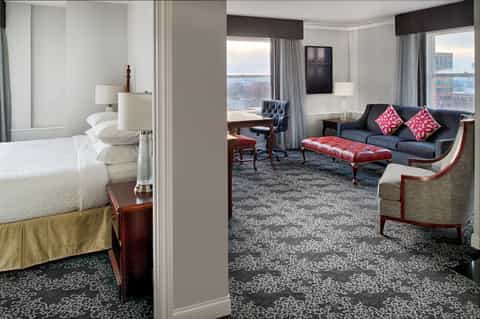 Luxury hotel suite with bedroom and living area featuring navy furniture and city views