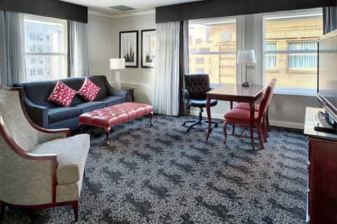 Upscale hotel suite with navy sofa, burgundy ottoman, desk, and floor-to-ceiling windows