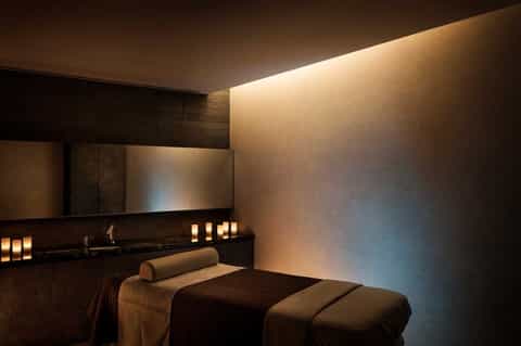 Modern spa treatment room with massage table, dark tile walls, and ambient lighting