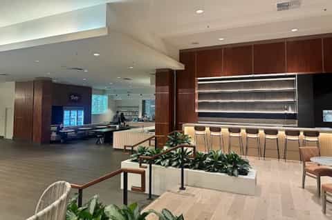 Modern hotel lobby with dark wood accents, illuminated bar, wooden stools, and contemporary seating