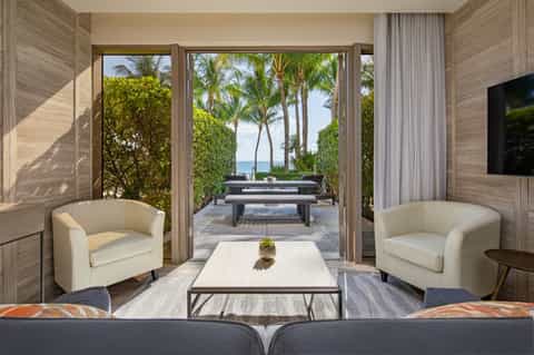 Beachfront suite interior with cream chairs, open terrace, ocean view, and tropical landscaping