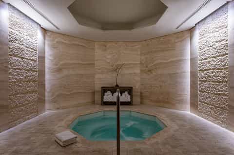 Spa steam room with marble walls and heated mineral pool in center